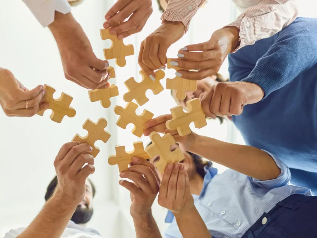 A diverse group of people holding wooden puzzle pieces together, symbolizing collaboration, problem-solving, and connection in ADHD couples group therapy.
