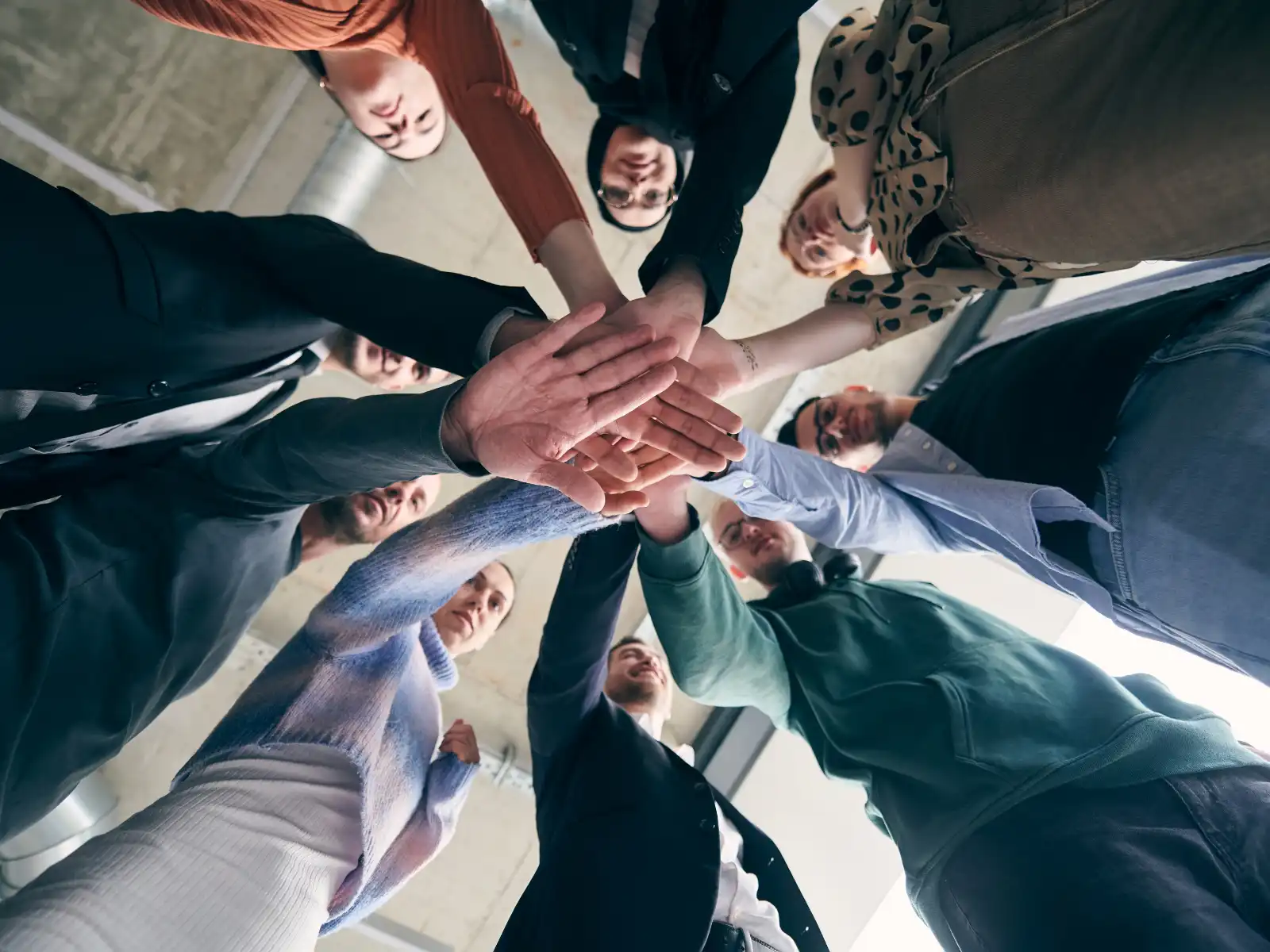 A diverse group of people standing in a circle, joining hands in the center as a symbol of unity and support during a couples group therapy session in Los Angeles.