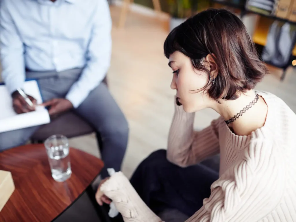 A young woman sits in deep thought during a therapy session, with a compassionate therapist taking notes, illustrating the emotional healing offered through EFT for couples in Los Angeles.