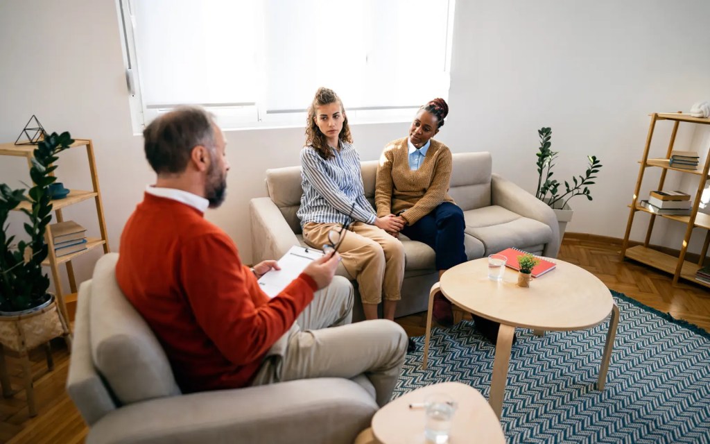 An interracial lesbian couple sitting on the couch during a couple's therapy session with a couples therapist