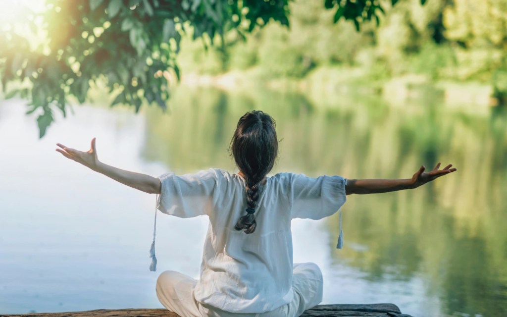 A woman sitting on the end of a pier on a lake with her arms out stretched symbolizing self development many individuals go on before starting couples therapy