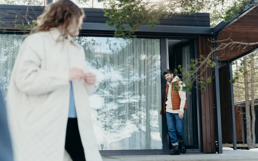 Sound-relationship-house-Gottman-method A woman smiling and turning around outside her house after seeing her partner exiting a door. The partner is making eye contact with the woman symbolizing the Gottman method's sound relationship house.