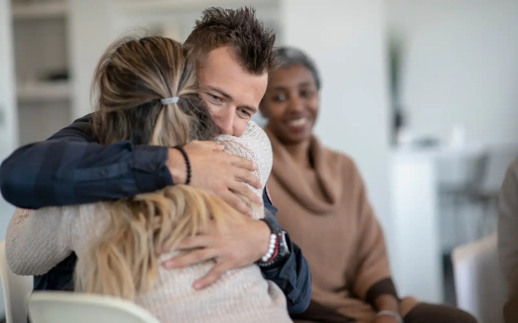 A couple hugging in front of their therapist when graduating EFT therapy and reflecting on their past sessions and journey