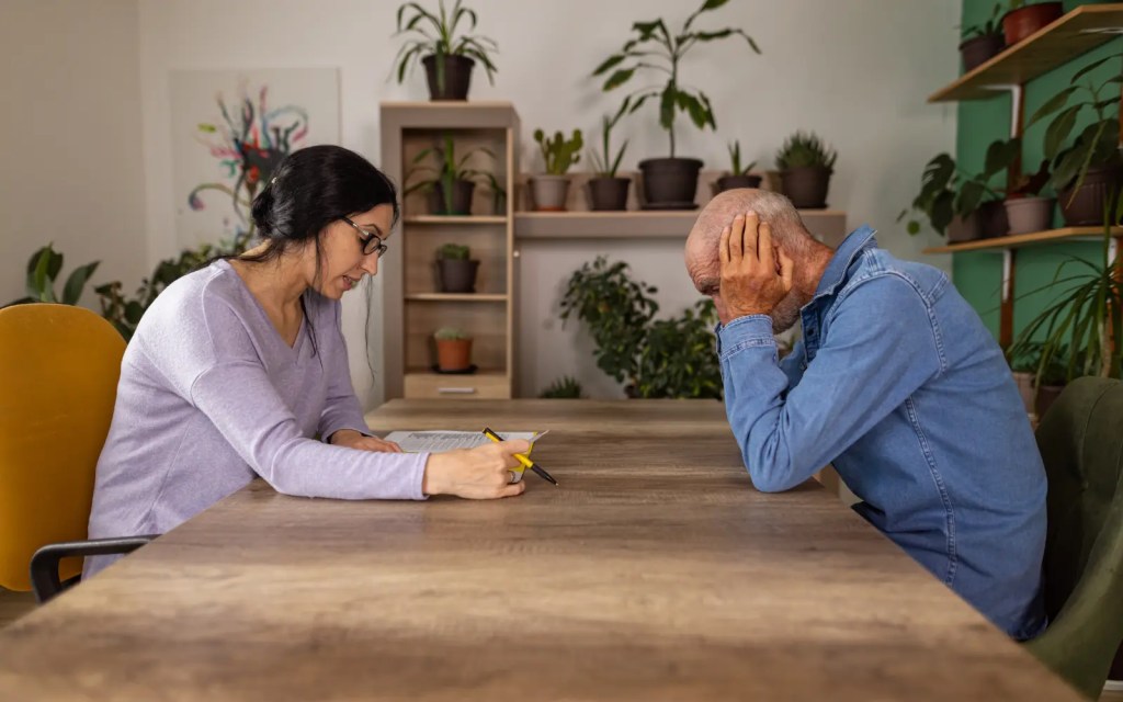 Anxiety-in-therapy A female therapist sitting across a table from a man with his head in his hands, representing anxiety in therapy