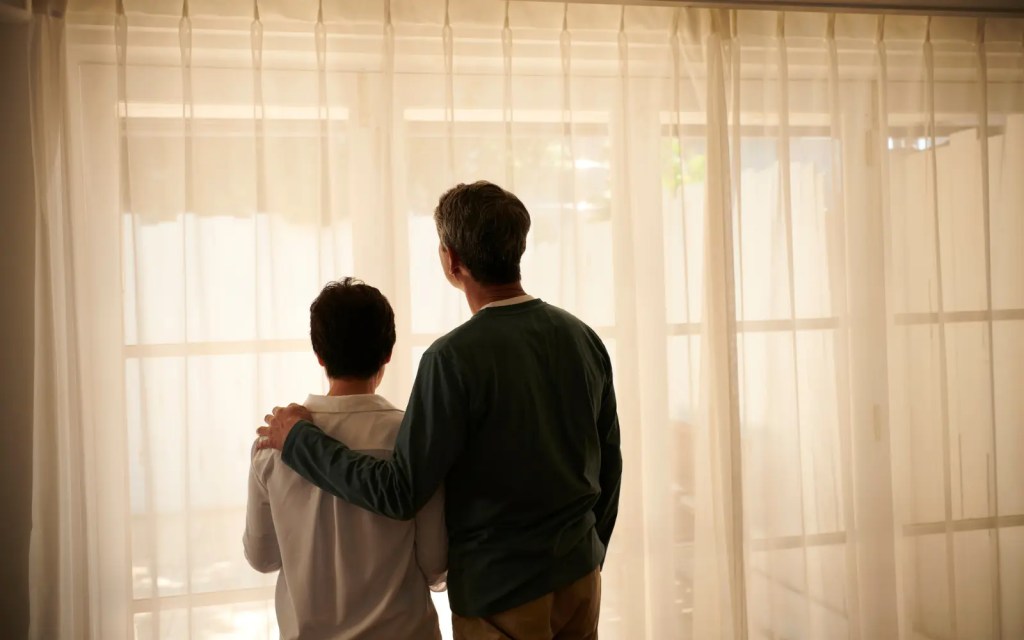 A couple looking out of a window, the man with his arm around the woman, representing emotional connection in couples therapy