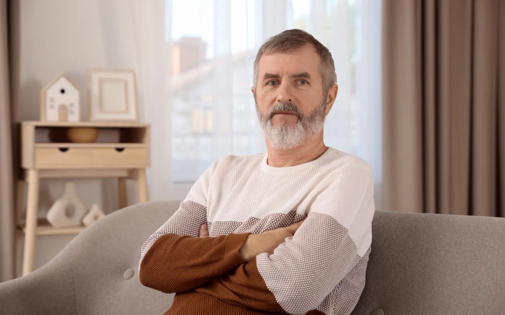 Body-language-in-therapy-in-Los-Angeles A man sitting on a couch with arms crossed, representing unconscious body language that an LA therapist may pick up