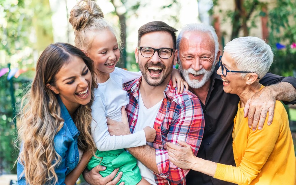 A multi-generational family smiling and laughing together outdoors, representing the impact of effective online therapy in Los Angeles families