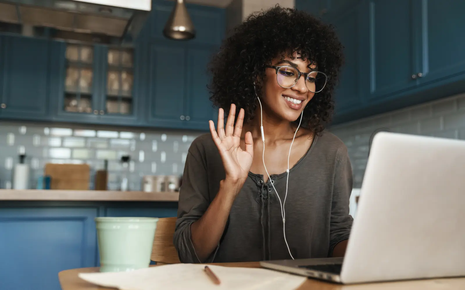 A woman in her kitchen smiling and waving at her laptop screen, representing getting support through Los Angeles online therapy