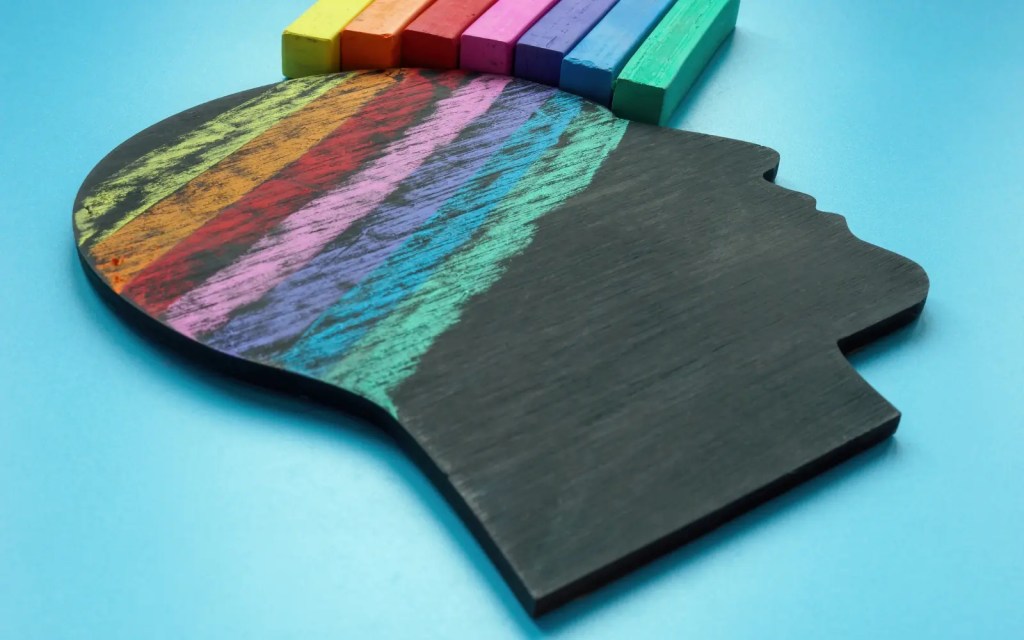 Neurodiverse-therapy-in-LA A black chalkboard in the shape of a human head's silhouette with a chalk rainbow drawn over the brain area, representing neurodiverse therapy in Los Angeles