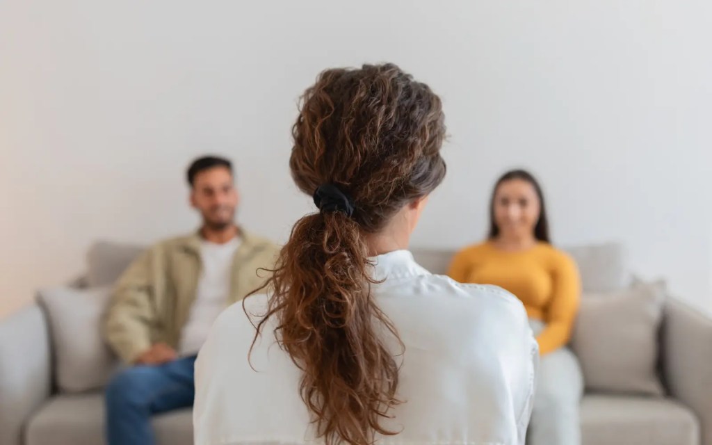 Therapist-managing-couples-in-therapy A couple in couples therapy in Los Angeles both looking at their therapist after an argument in session