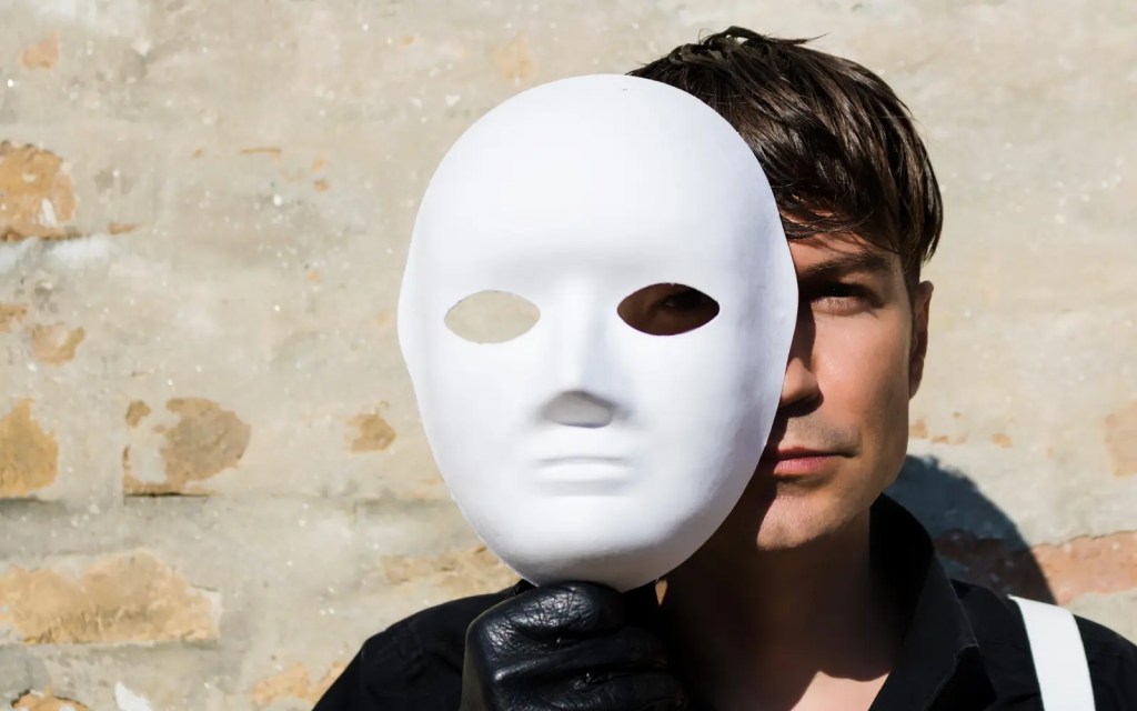 A man holding up a white mask, representing individual masking of ADHD symptoms
