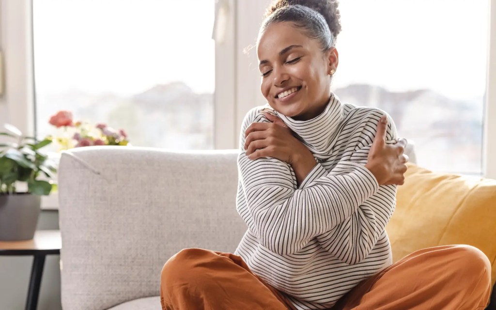 A smiling woman with her arms wrapped around herself, representing self-compassion from GGPA's Los Angeles therapy for neurodiverse folx