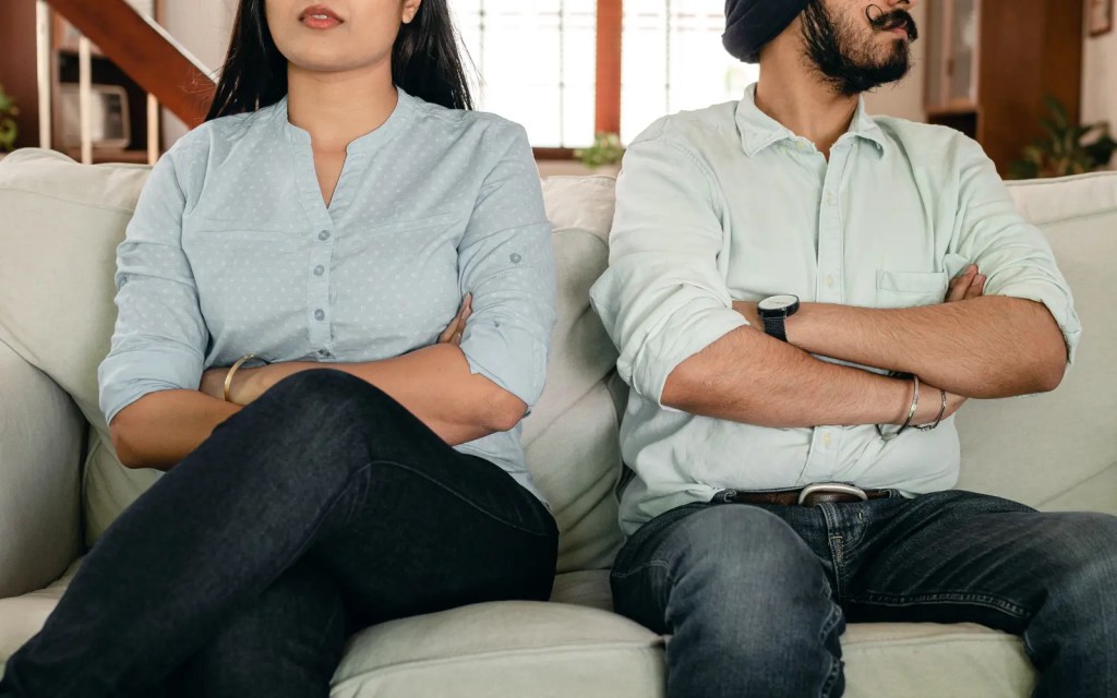 A couple after an argument sitting on a couch with arms folded, representing the overwhelm the non-ADHD partner can face in neurodiverse relationships