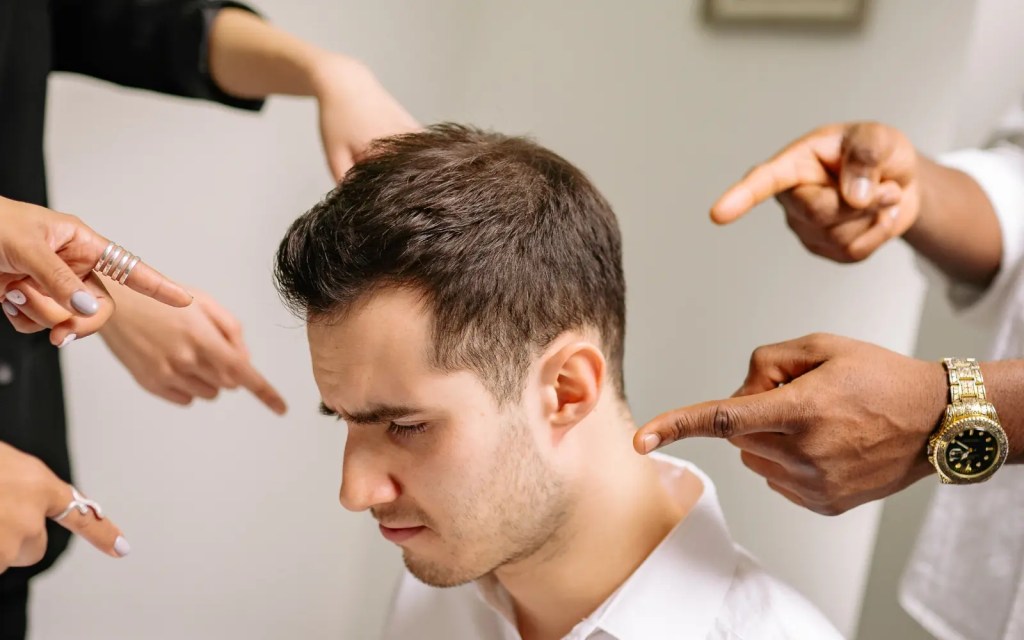 A man surrounded by fingers pointing at him, representing the self-criticism many ADHDers feel regularly
