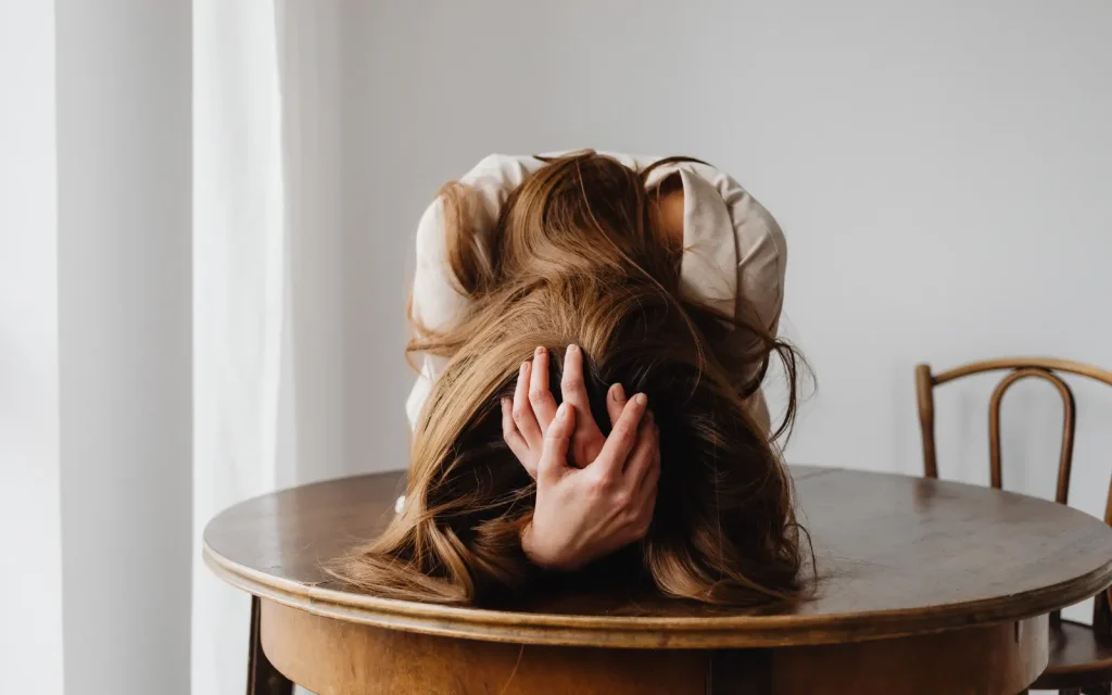 A woman holding her head face down on the table, representing the question "What are ADHD spouse burnout symptoms?"