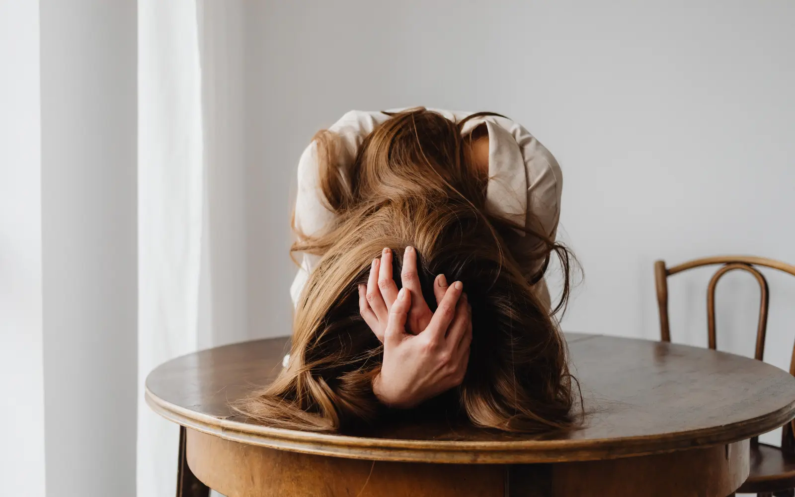 A woman holding her head face down on the table, representing the question "What are ADHD spouse burnout symptoms?"